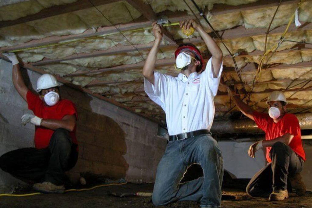 Three masked men in red shirts work on insulation in a crawl space as part of a mold removal service in San Francisco, CA.